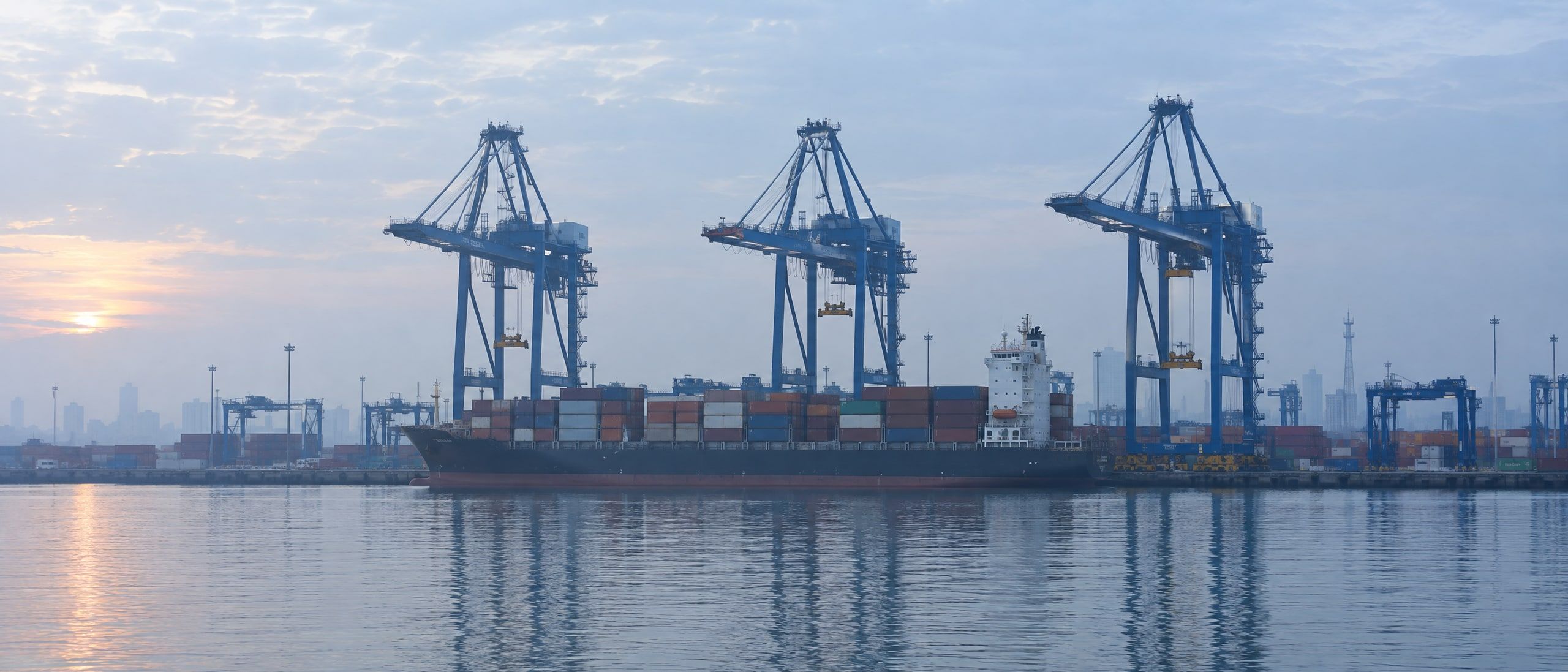 Container cranes above a berthed ship at Tanjung Priok port at dawn